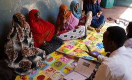 Mothers sit together during a mental health and psychosocial support session led by mental health promoters. Health workers guide discussions on coping with stress and caring for young children after displacement.