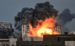 People standing on a rooftop watch as a ball of fire and smoke rises above a building in Gaza City on October 7, 2023 during an Israeli air strike that hit the Palestine Tower building.