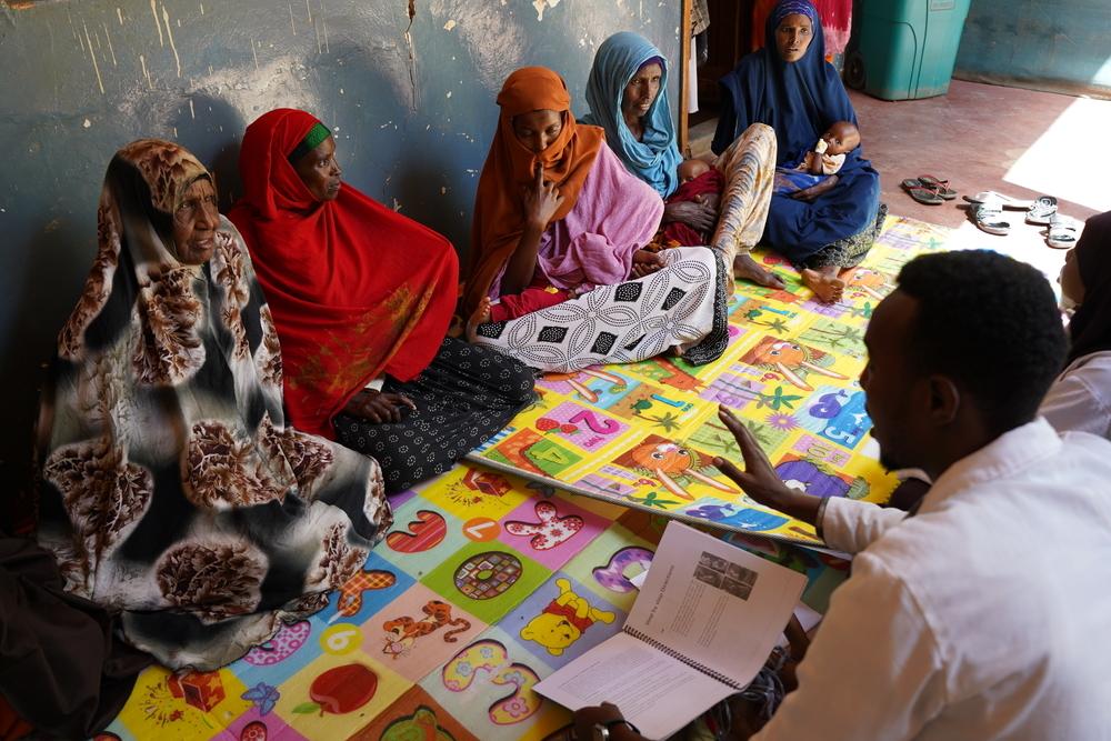 Mothers sit together during a mental health and psychosocial support session led by mental health promoters. Health workers guide discussions on coping with stress and caring for young children after displacement.