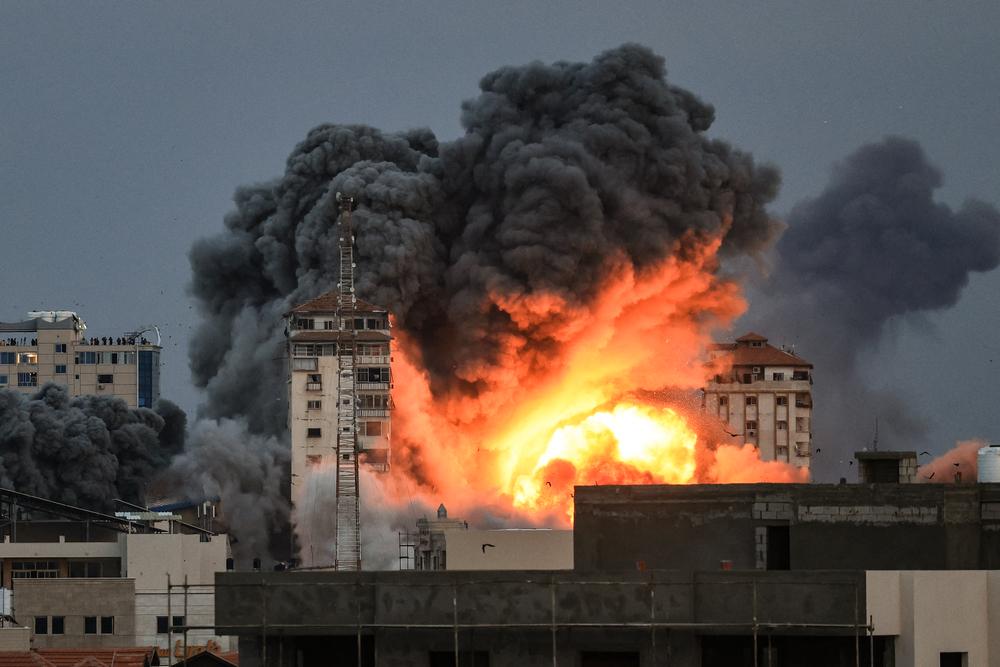  People standing on a rooftop watch as a ball of fire and smoke rises above a building in Gaza City on October 7, 2023 during an Israeli air strike that hit the Palestine Tower building.