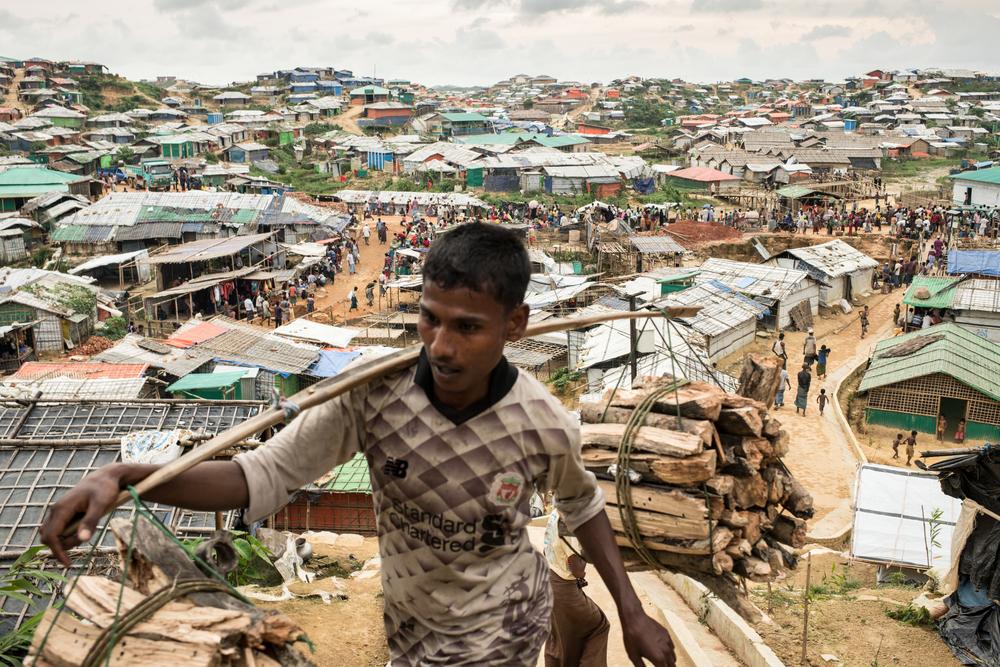 A Rohingya man carries wood through the Kutupalong- Balu Khali mega camp. Cox’s Bazar District, Bangladesh. [© Robin Hammond/NOOR ]