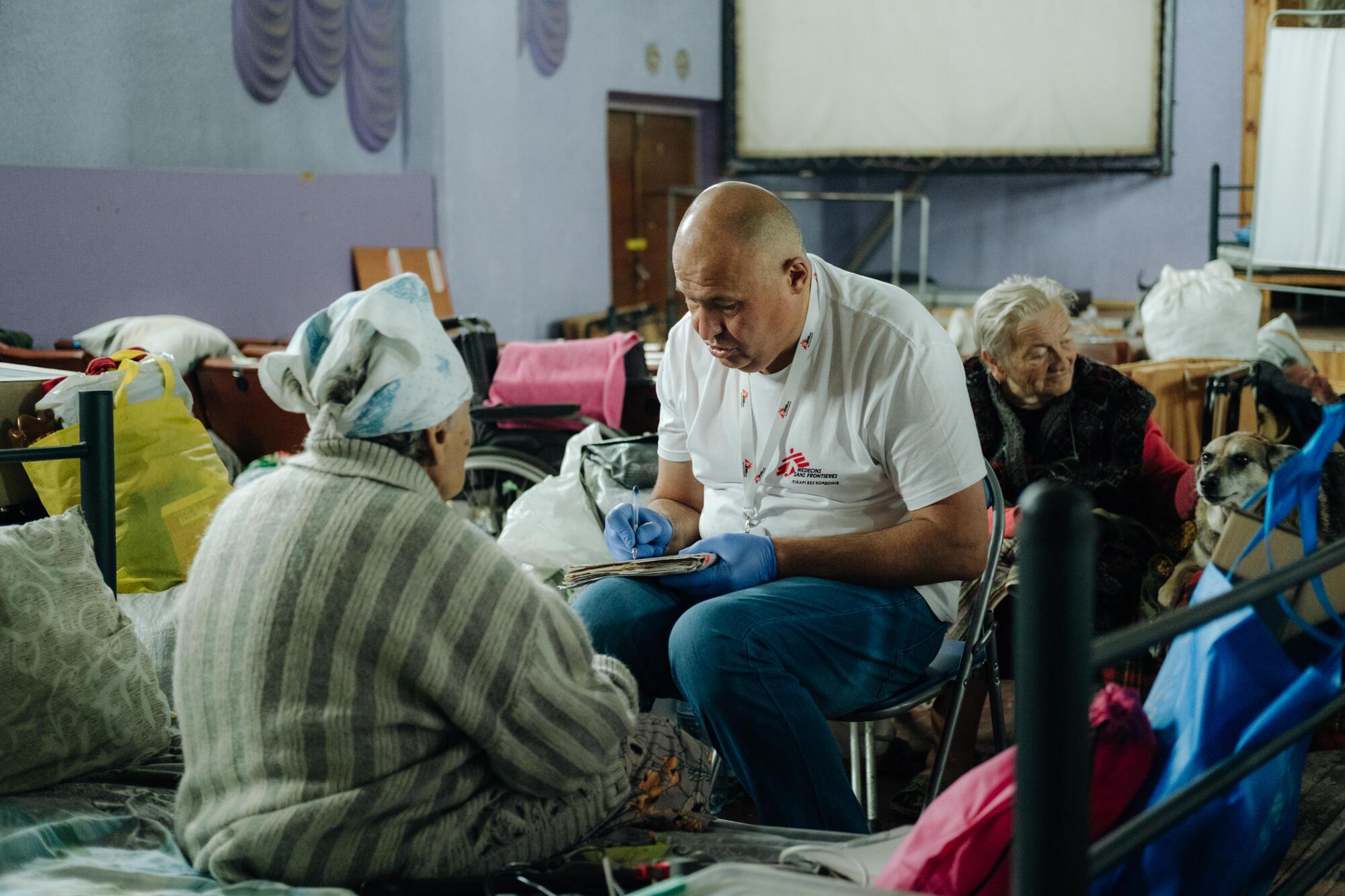 Inside the transit centre in Dnipropetrovsk region, an MSF staff member sits with people who have been displaced from areas near the frontlines. MSF staff examine patients and provide psychological support in this centre. Ukraine, July 2025.