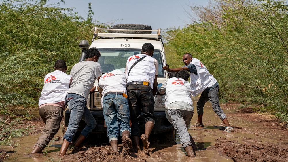 MSF staff pushing a vehicle that got stuck in the mud as a result of the flooded paths, on the way to one of the Health Centers where MSF does the outreach activity, doing MUAC and providing plumpy’nuts for children under 5
