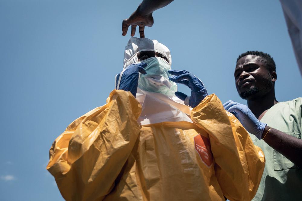 MSF colleagues assist a hygienist in donning personal protective equipment (PPE) before she enters Sayo Health Centre in Mongbwalu to decontaminate several rooms.
