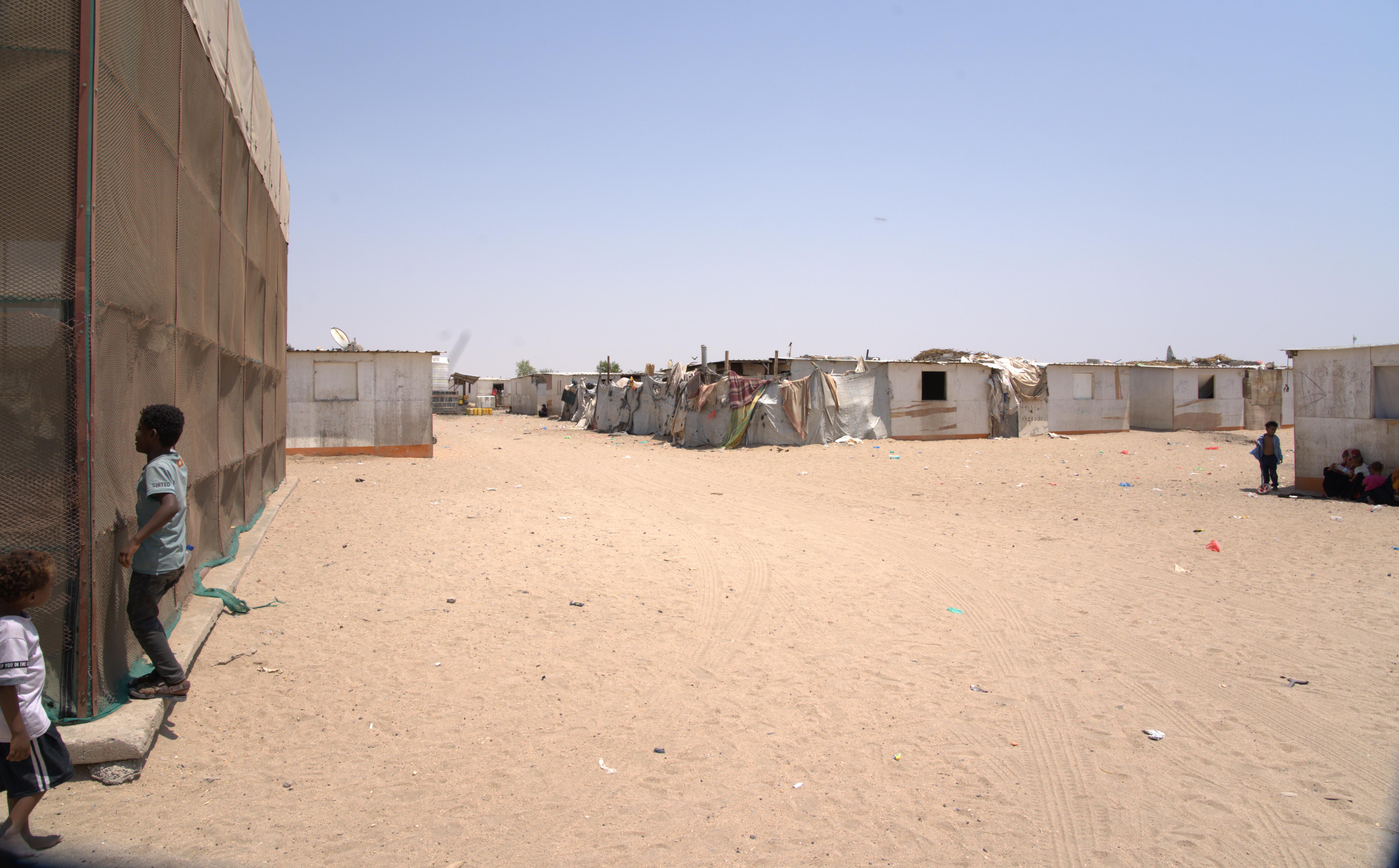 Children stand outside watching a vaccination team that has arrived at a camp for displaced people in Ateera 2, Tuban district, Lahj governorate, Yemen, 5 May 2026. The camp is located far from the nearest health facility, and many residents are displacing families living in very difficult economic conditions.