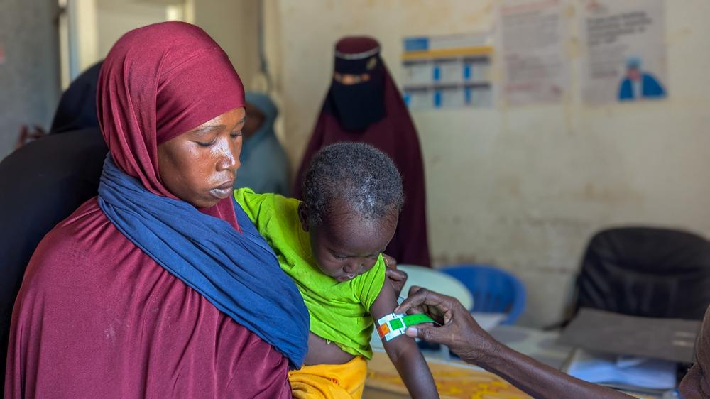 A nurse measures the mid-upper arm circumference of a child during a nutrition screening at the triage area. The colour-coded band is the quickest way to identify acute malnutrition, and a reading in the red range indicates a severe case needing immediate treatment.